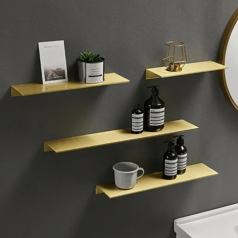 Set of three gold floating wall shelves holding decor and toiletries against a dark wall.