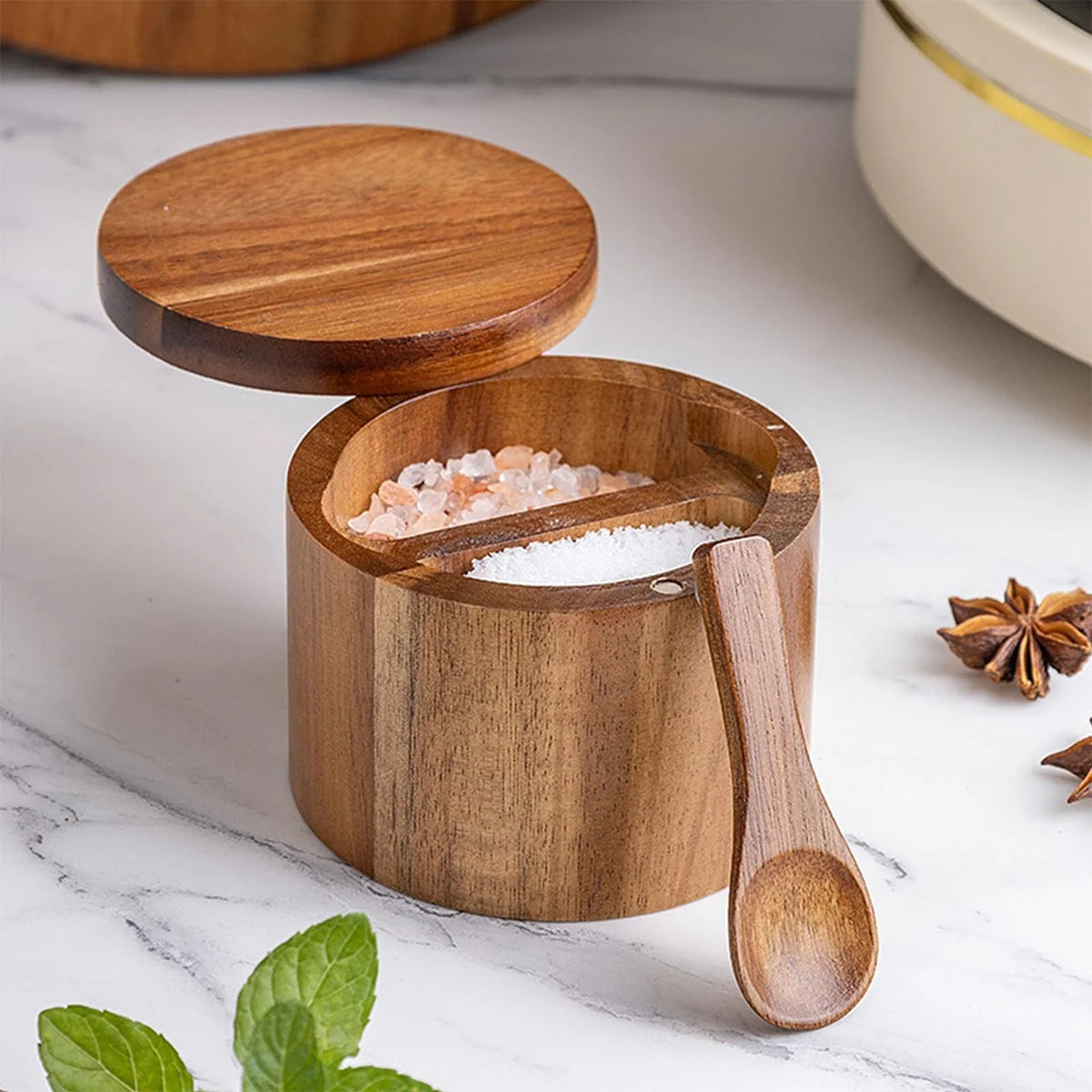 Wooden salt cellar with lid and spoon filled with pink salt.