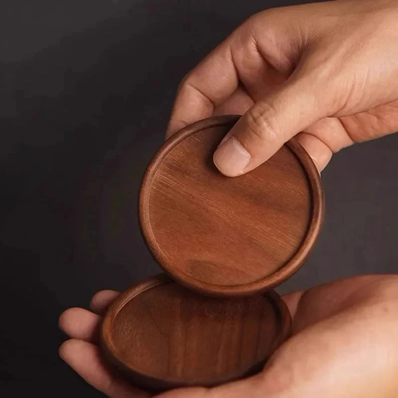 Hands holding a pair of smooth round dark wooden coasters.