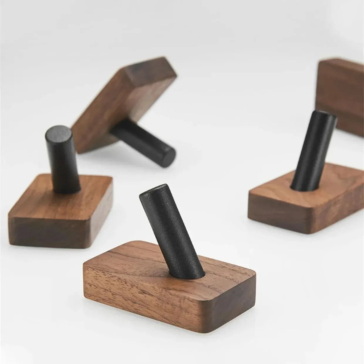 Several rectangular wood hooks with black cylindrical pegs, arranged on a white surface.