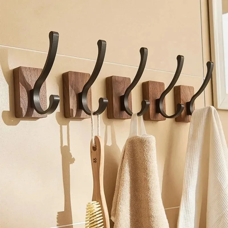 A row of five wood hooks with black metal, curved arms, holding towels and a brush.