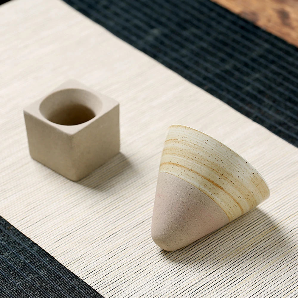 Textured ceramic cone coffee cup next to a square stone holder on a striped placemat.