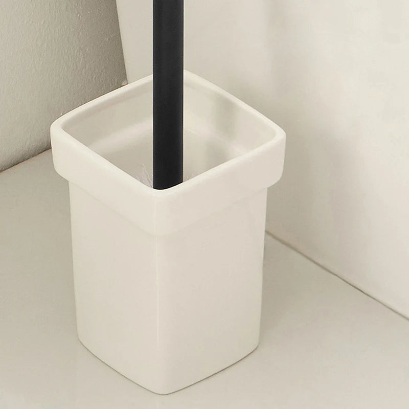 A white ceramic toilet brush holder with a black-handled brush inside