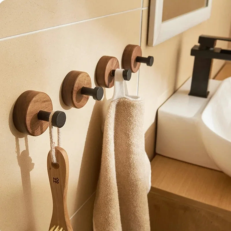 Four round wood hooks with black pegs in a bathroom setting, holding a towel and a brush.
