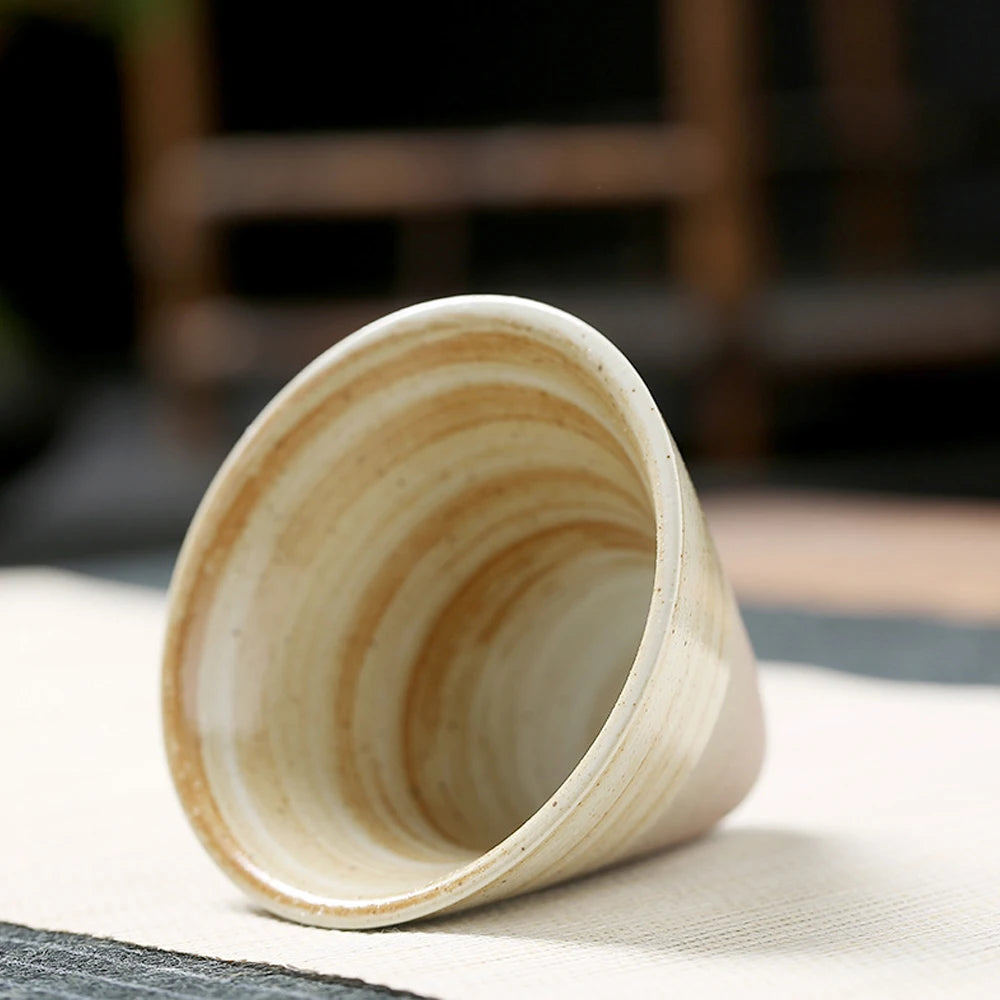 Light-colored, swirled ceramic cone coffee cup on a white surface.